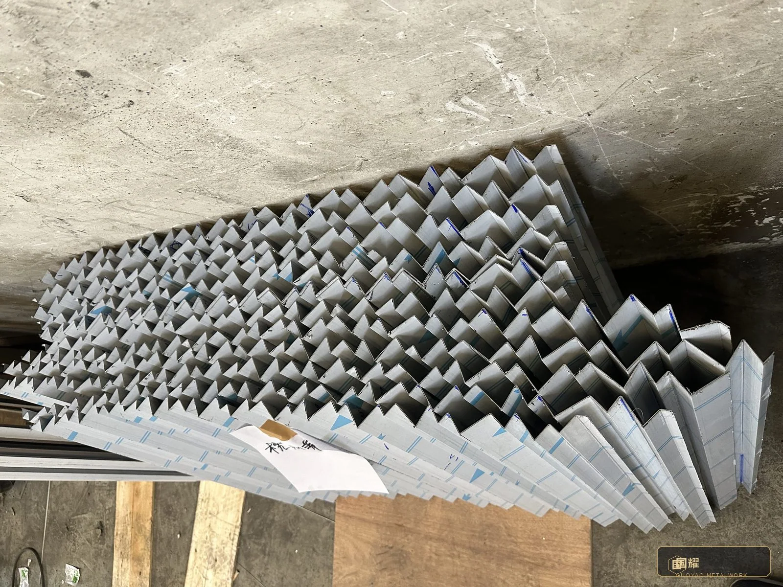 Fluted panels in full run off the forming line — deep, even, parallel flutes in the approved silver, the signature surface of the whole facade.